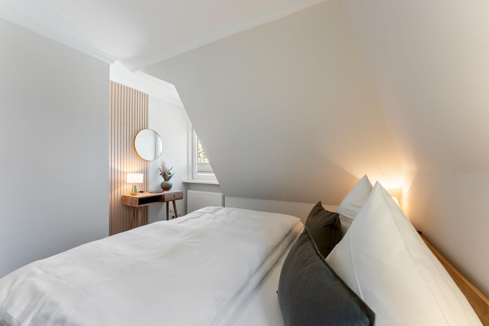 Bedroom with sloped ceiling, bed, nightstand, and mirror.