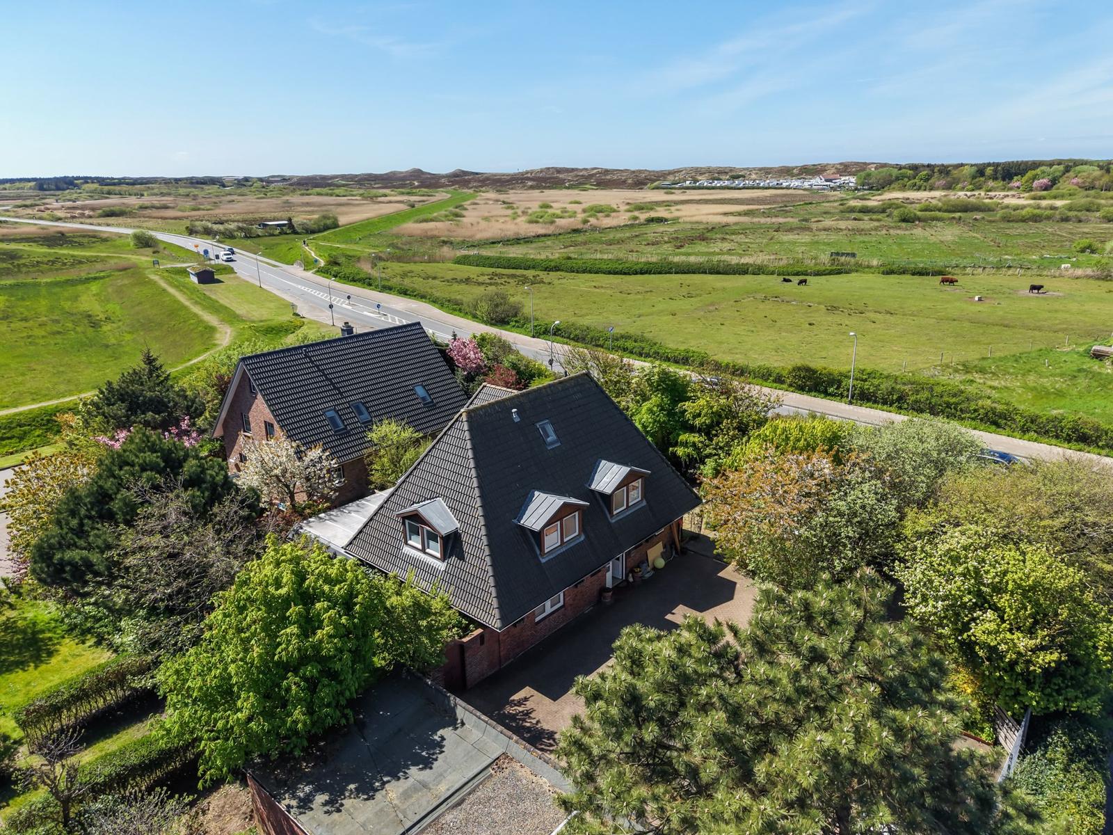 Haus mit Dachgauben und Garten, umgeben von Wiesen und Bäumen.