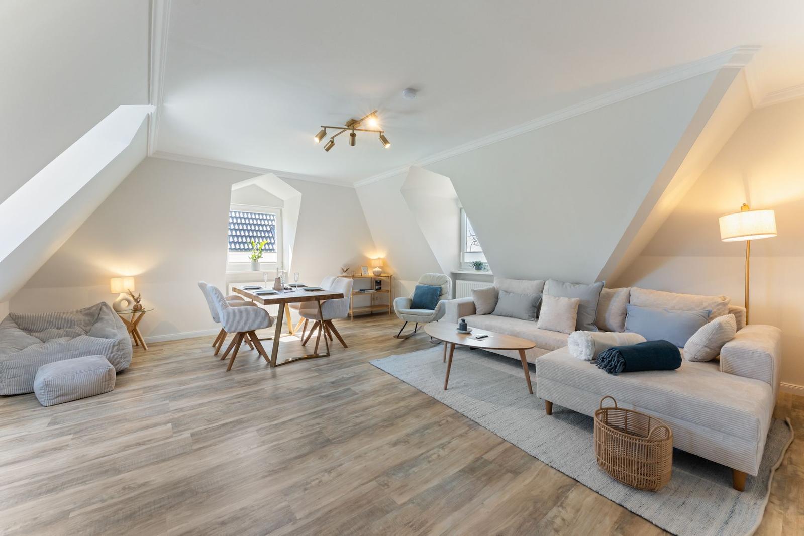 Wohn- und Essbereich mit Sofa, Tisch und Stühlen unter schrägen Dachschrägen.