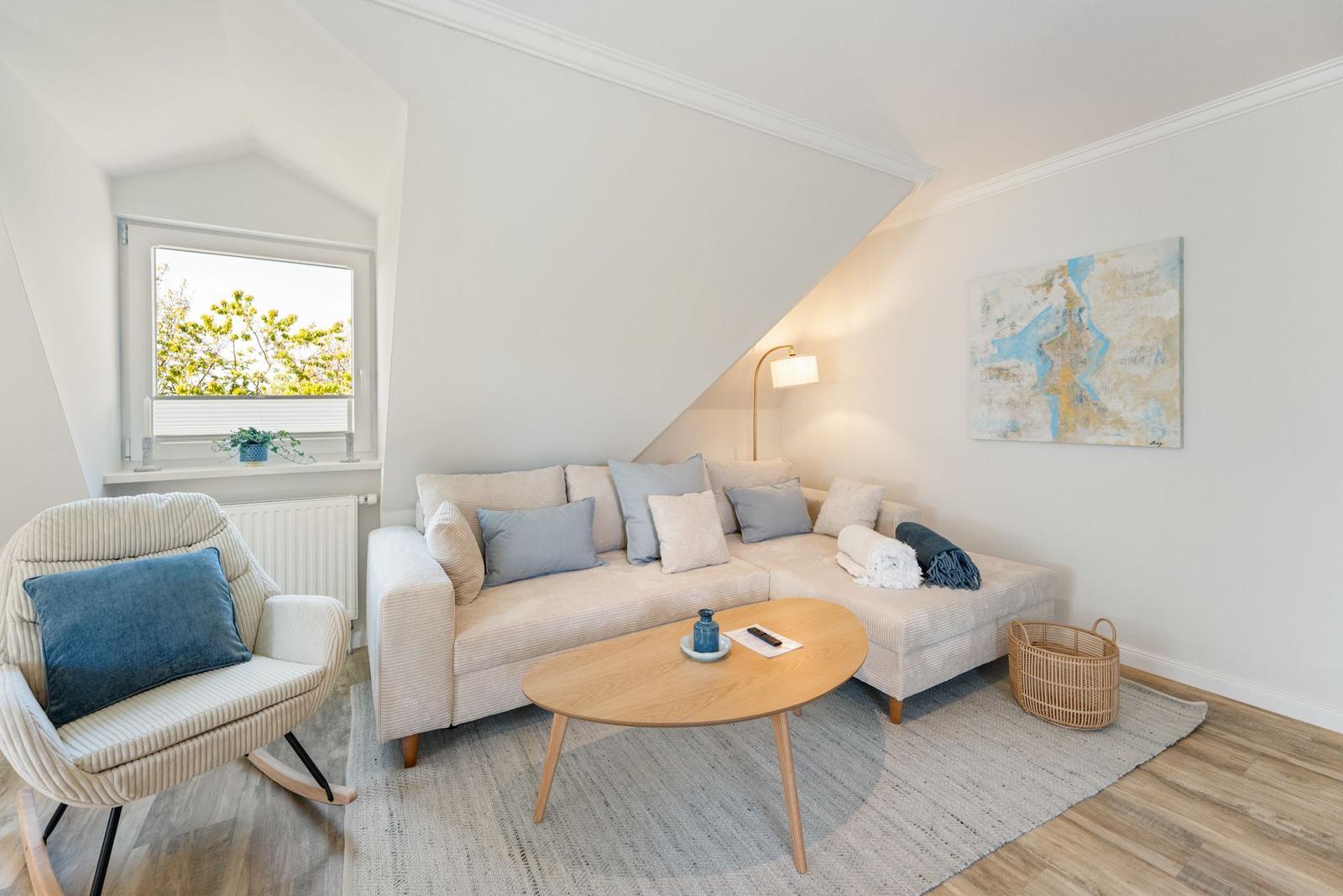 Wohnzimmer mit Sofa, Sessel und Tisch unter schrägem Dach