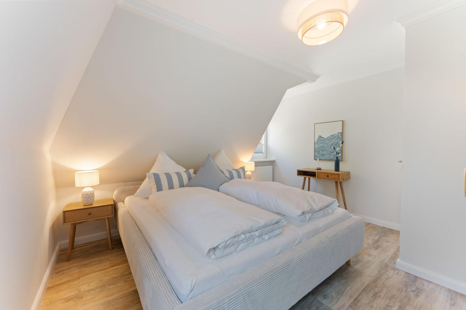 Schlafzimmer mit Doppelbett, Nachttisch und Wandbild. Holzfußboden und schräges Dach.