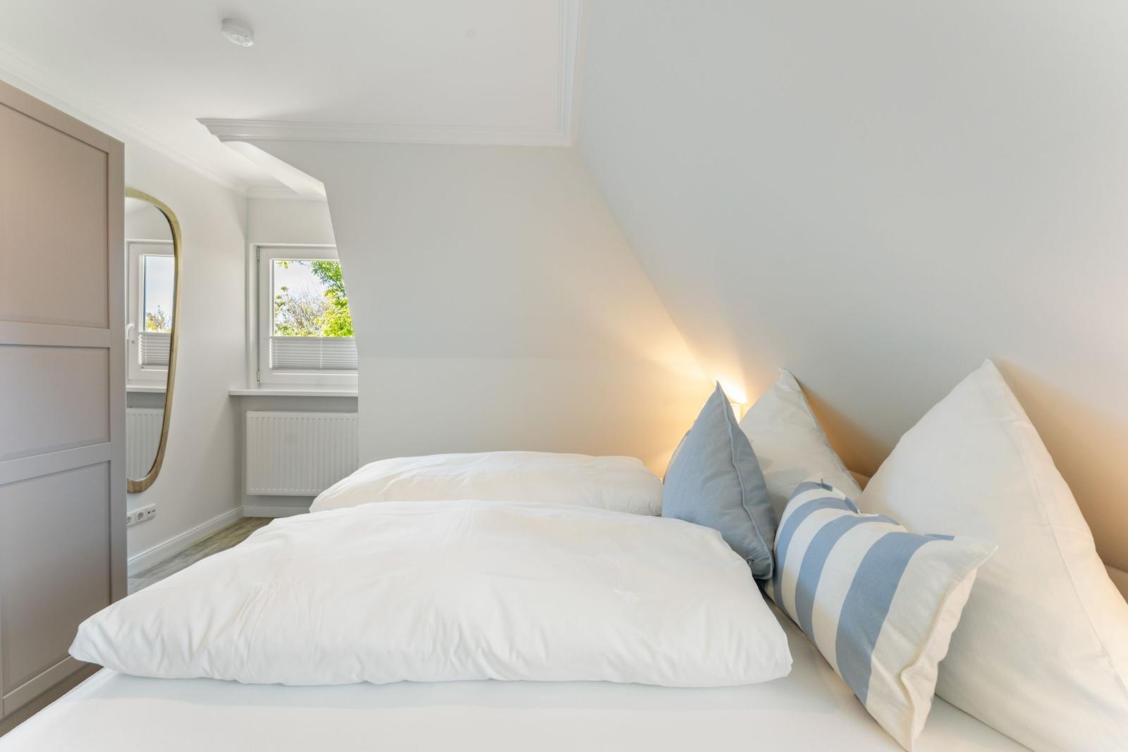 Schlafzimmer mit Dachschrägen, Bett mit Kissen und Fenster.