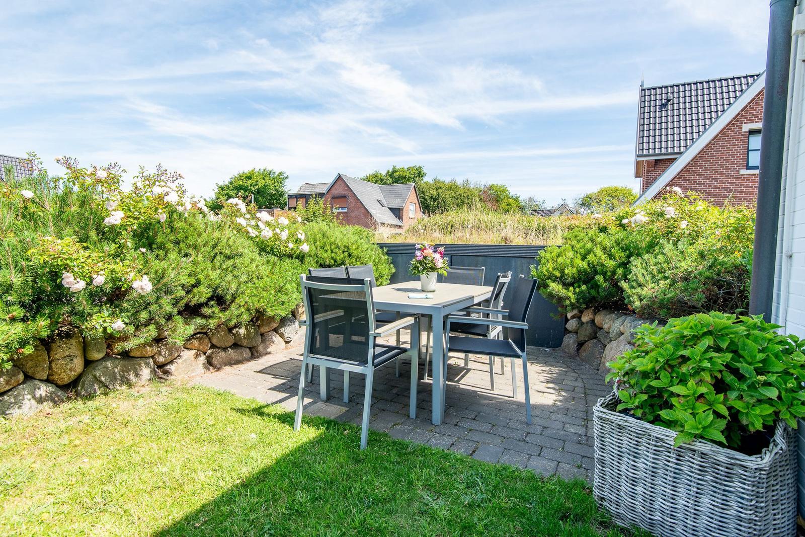 Terrasse mit Tisch und Stühlen, umgeben von Grünflächen und Sträuchern.