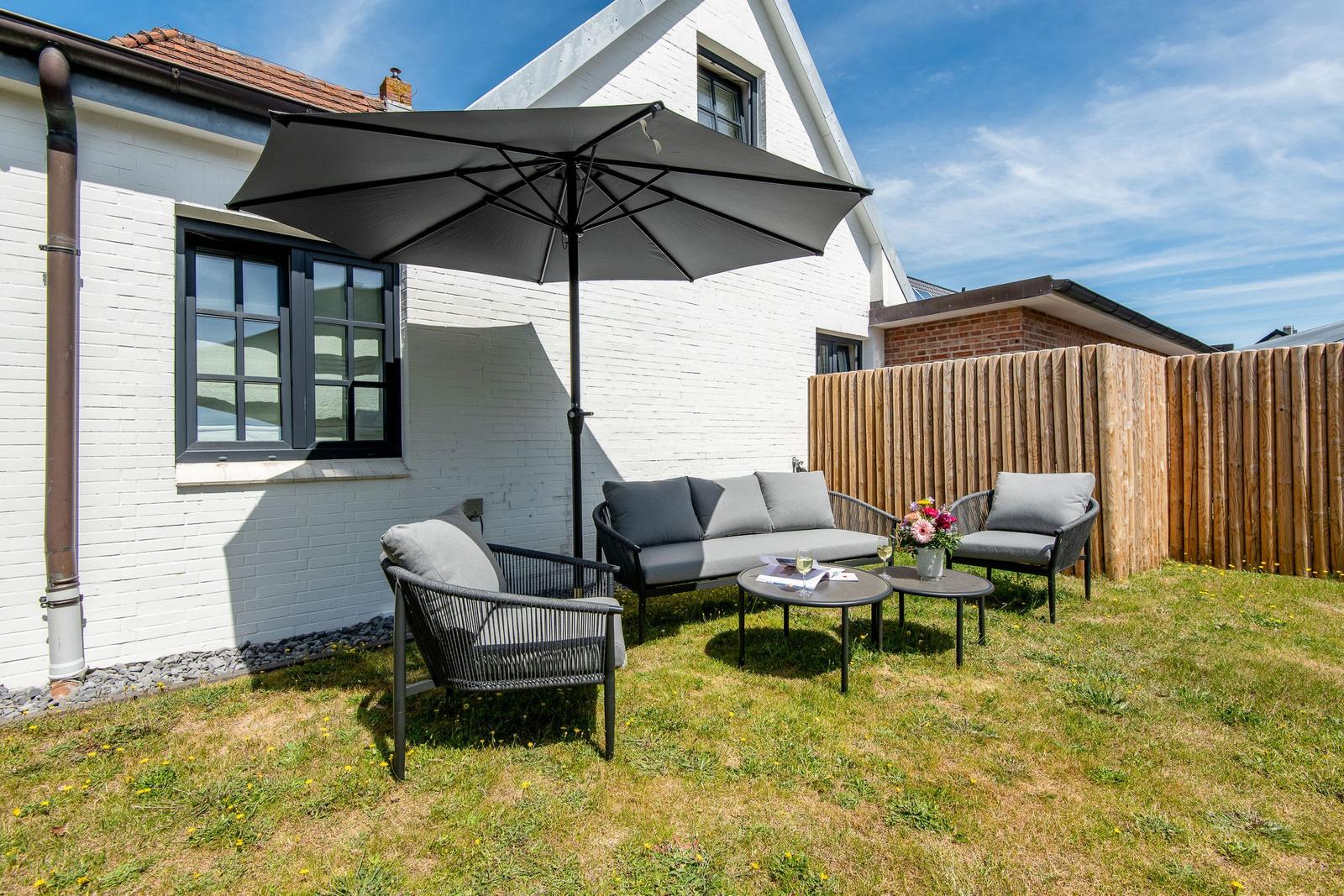 Hinterhof mit Sitzgruppe, Sonnenschutz und Blumenarrangement.