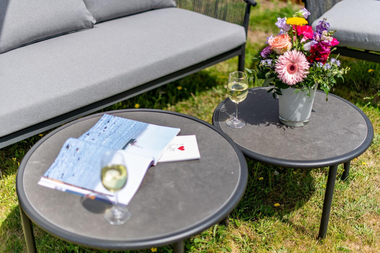 Zwei runde Tische mit Wein, Blumen und Broschüren im Garten.