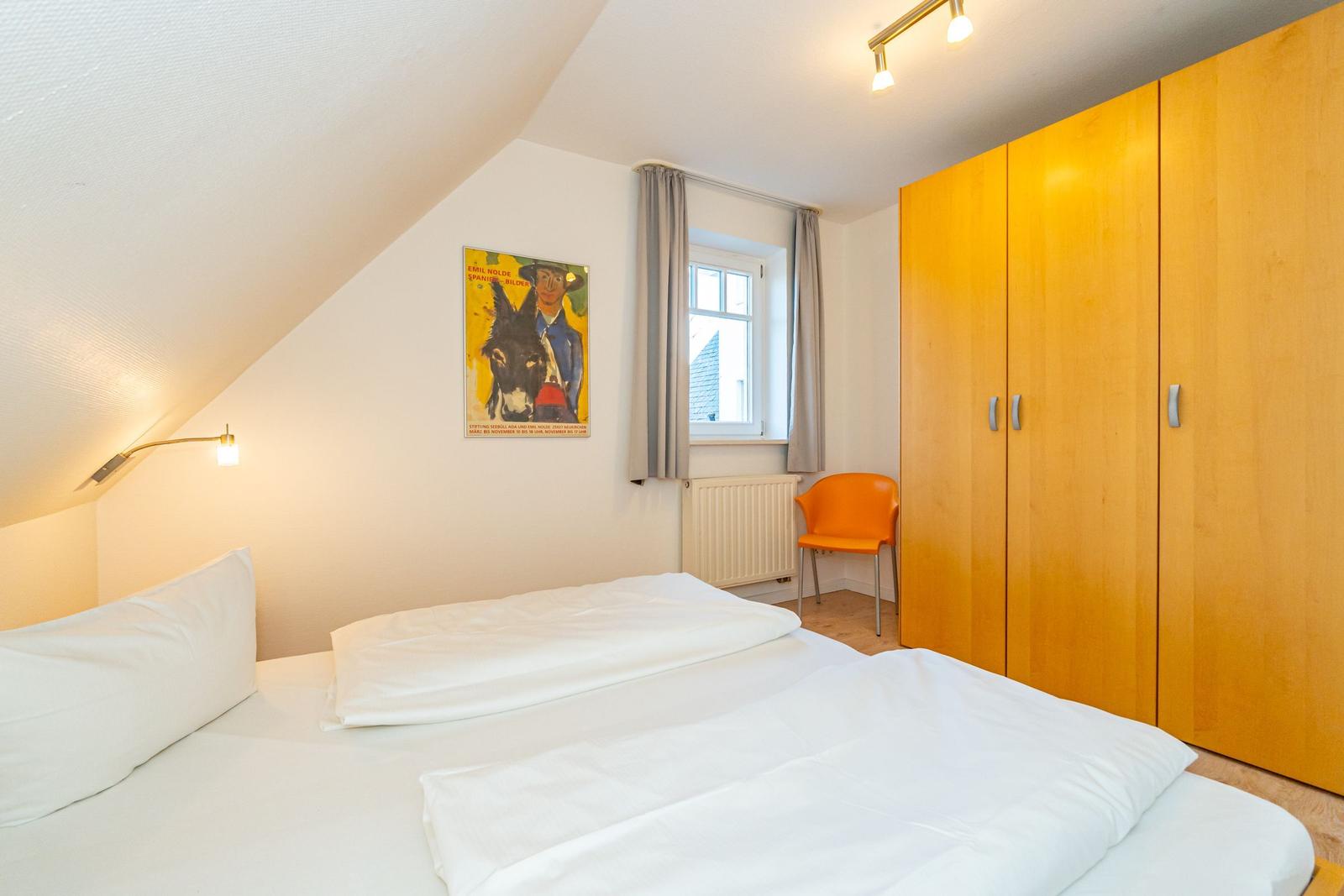 Schlafzimmer mit Doppelbett, Holzschrank und Fenster mit Vorhängen.