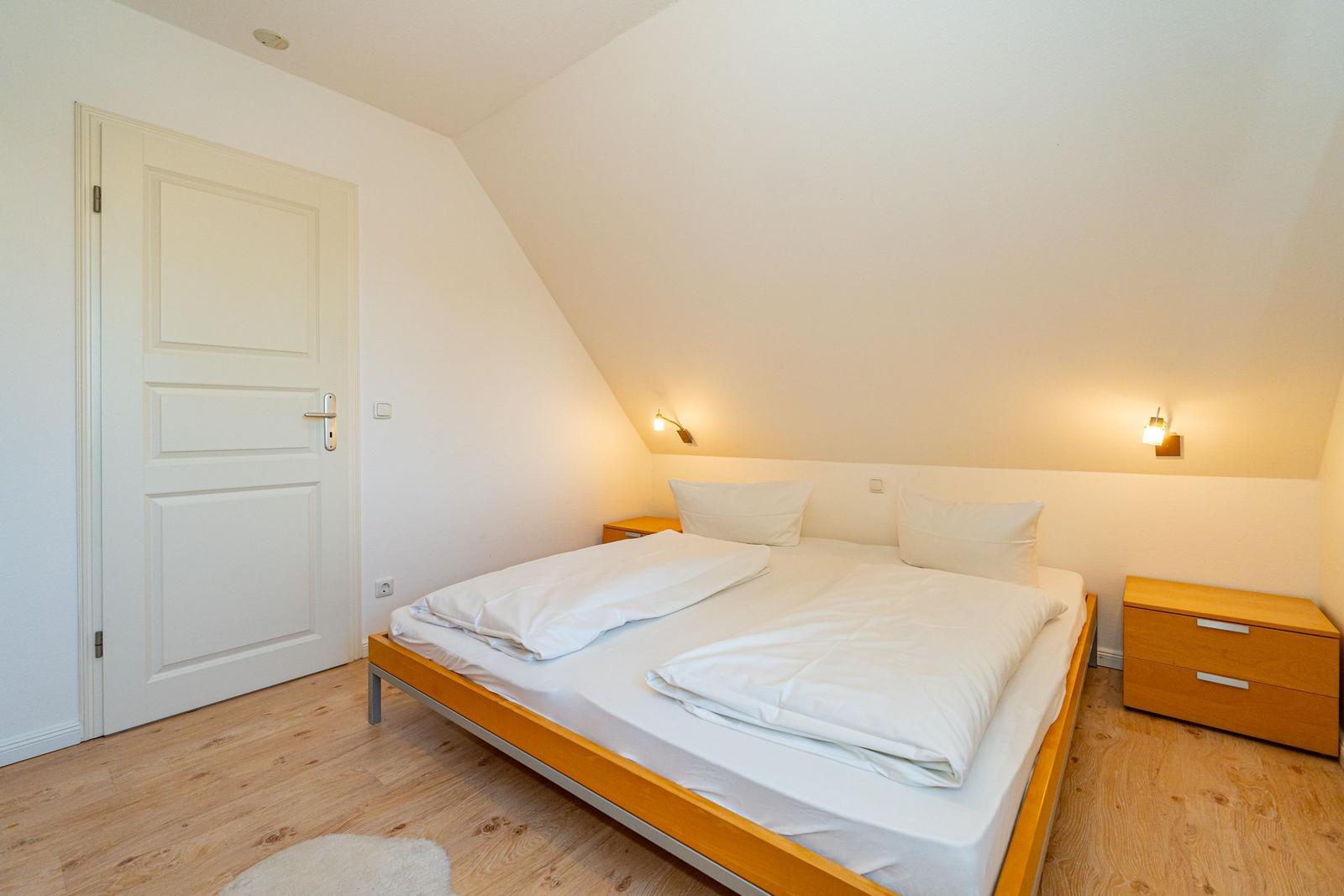 Schlafzimmer mit Doppelbett, Holzboden und Nachttischen an der Wand.