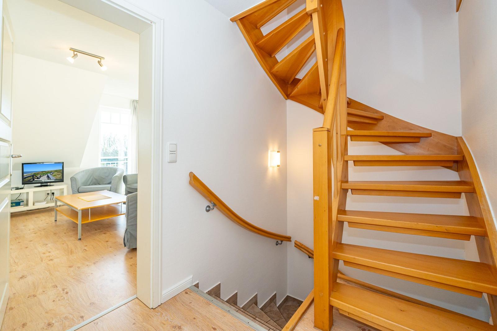 Holzgetreppe führt zur Wohnung. Im Hintergrund ist Wohnzimmer mit Sofa und Fernseher.