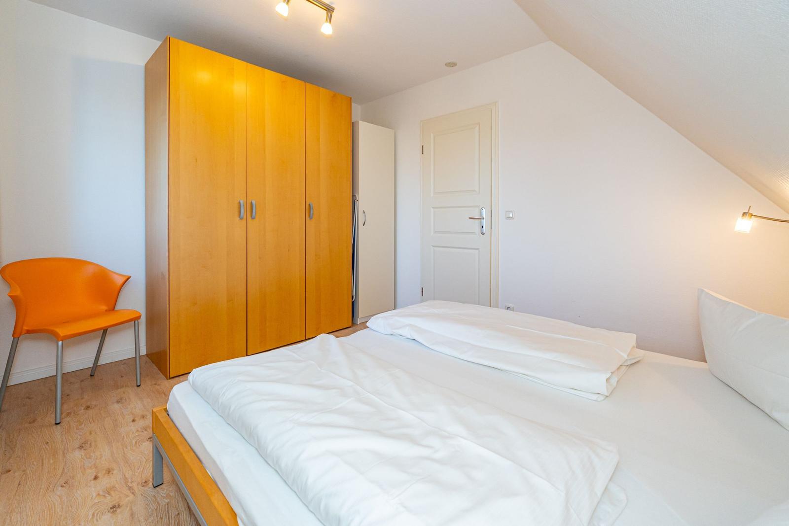 Schlafzimmer mit Bett, Kleiderschrank und Stuhl. Dachschrägen-Decke und Holzboden.