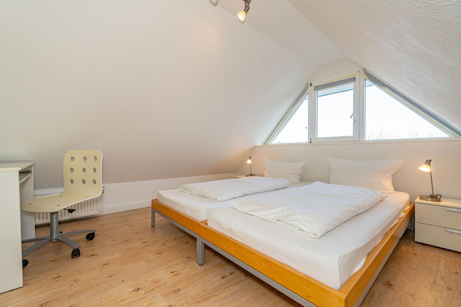 Schlafzimmer mit Doppelbett, Schreibtisch und Fenster unter Dachschrägen.