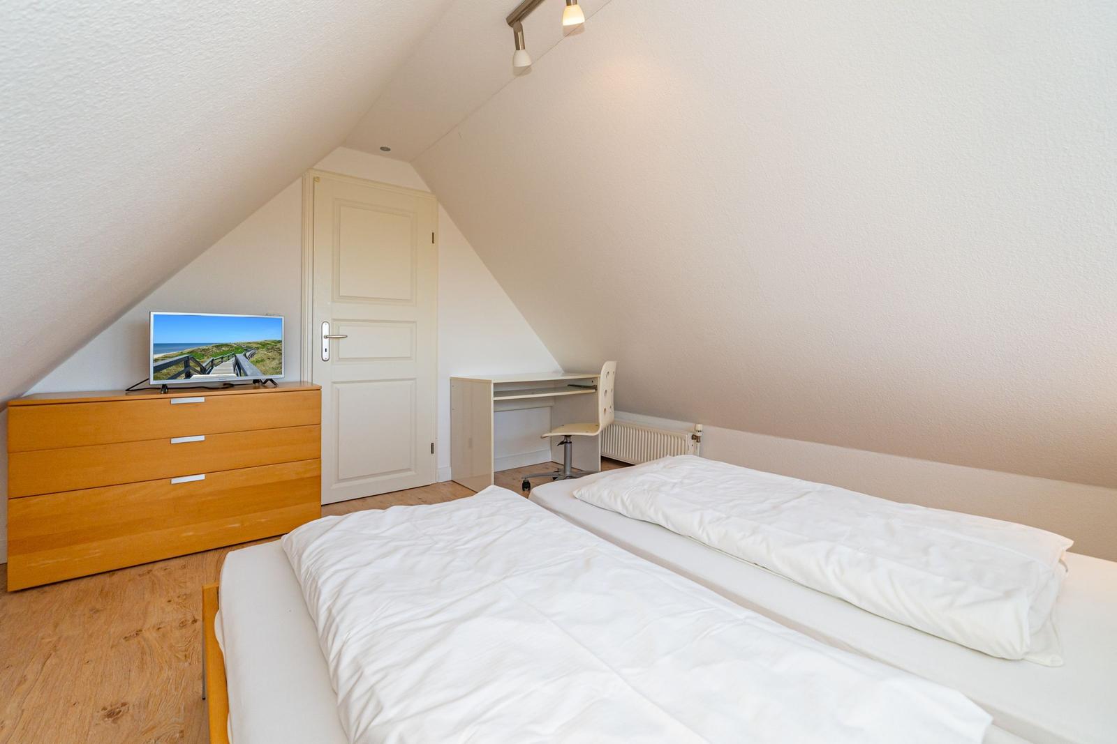 Schlafzimmer mit Doppelbett, Schreibtisch und Fernseher auf Schrank.