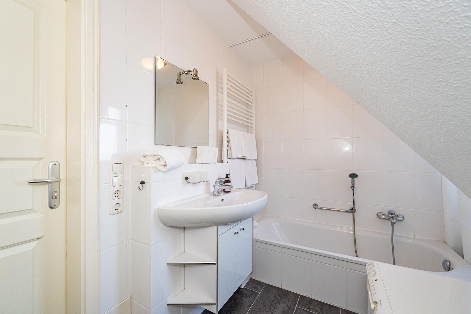 Badezimmer mit Badewanne, Waschbecken und Spiegel. Dachschrägen und weiße Fliesen.