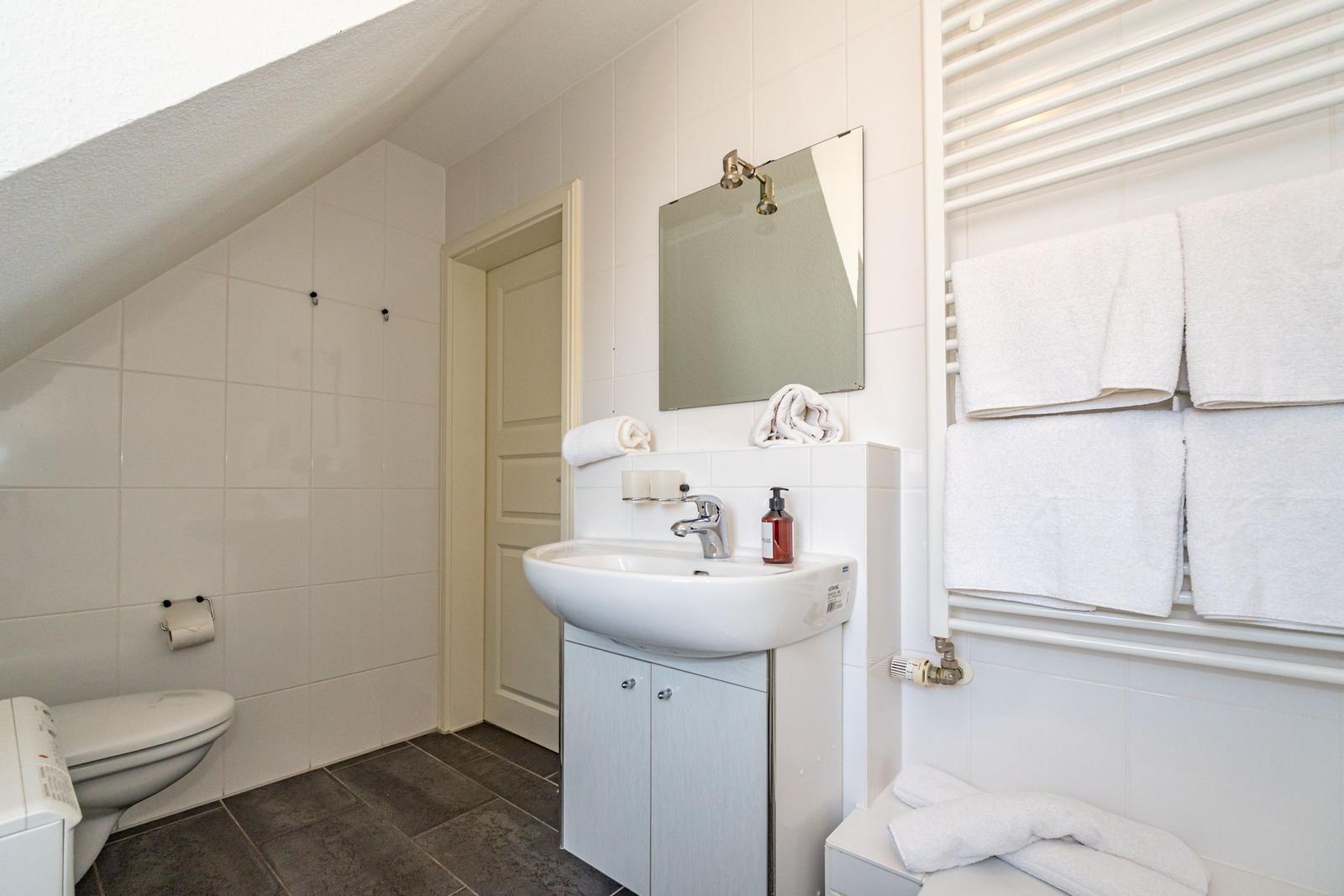 Badezimmer mit Waschbecken, Spiegel, Toilette und Handtuchheizung.