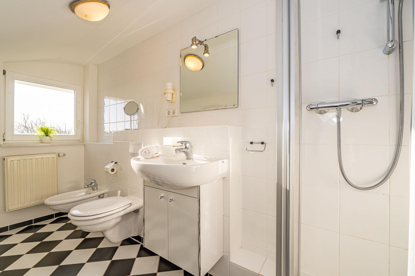 Badezimmer mit Dusche, Waschbecken und Toilette. Schwarzes und weißes Fliesenmuster.