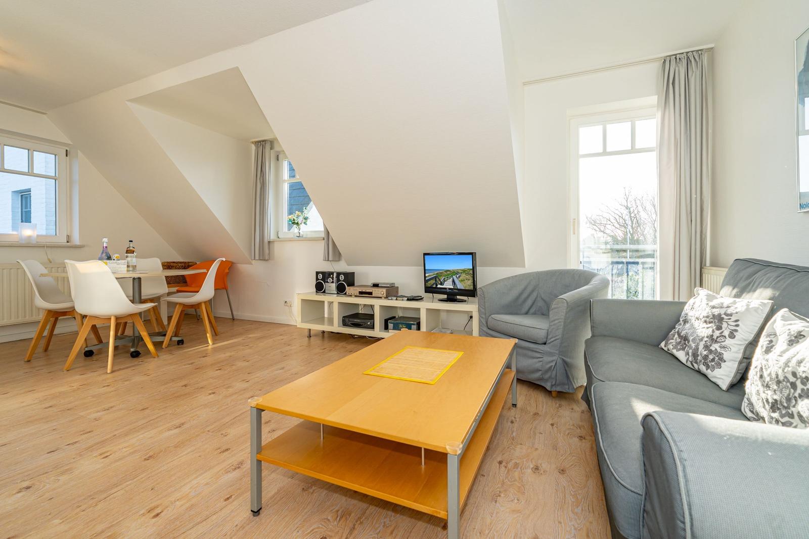 Wohn- und Essbereich mit Sofa, Couchtisch und TV. Holzboden und große Fenster.