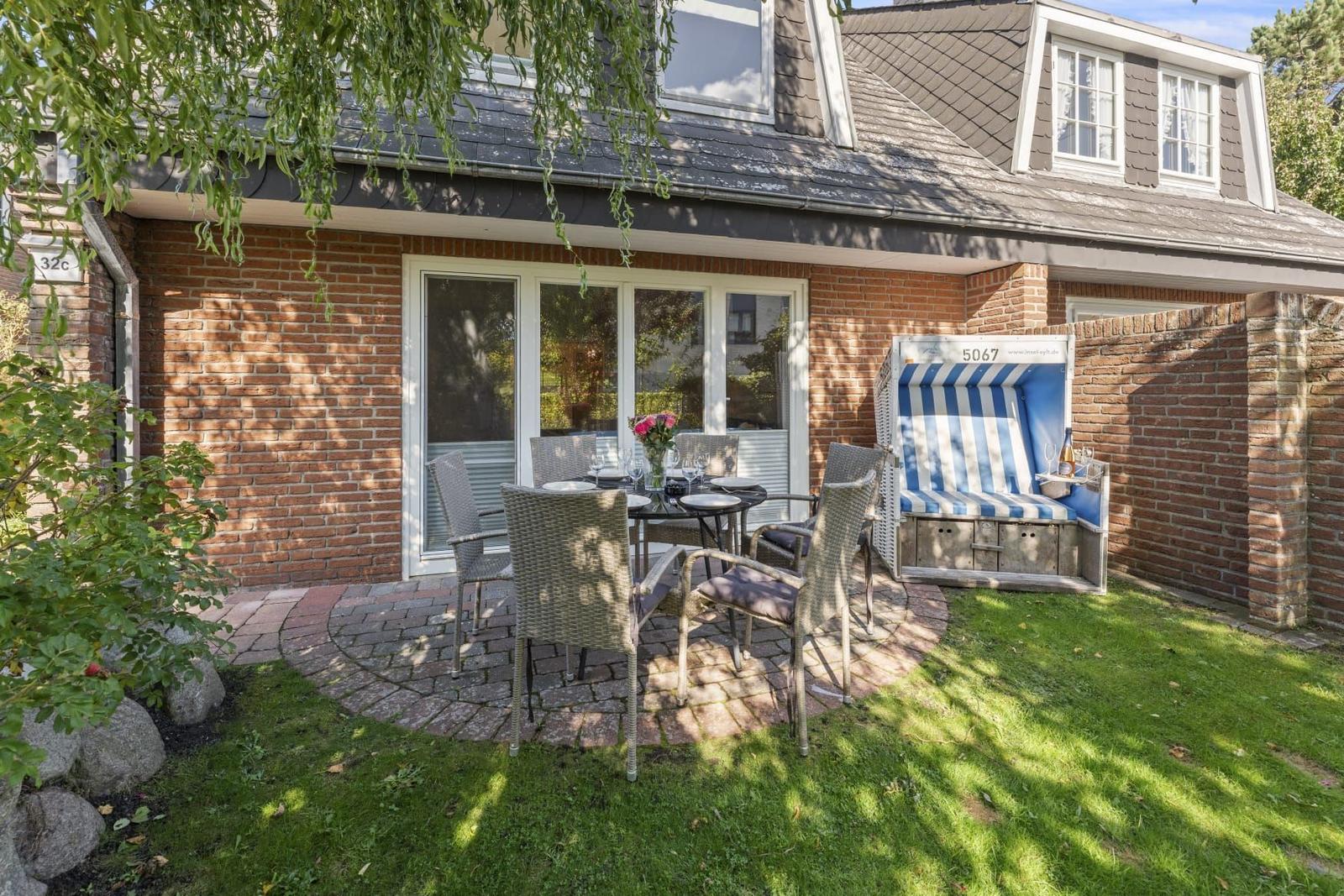 Terrasse mit Tisch, Stühlen und Strandkorb neben Haus mit Ziegelfassade.