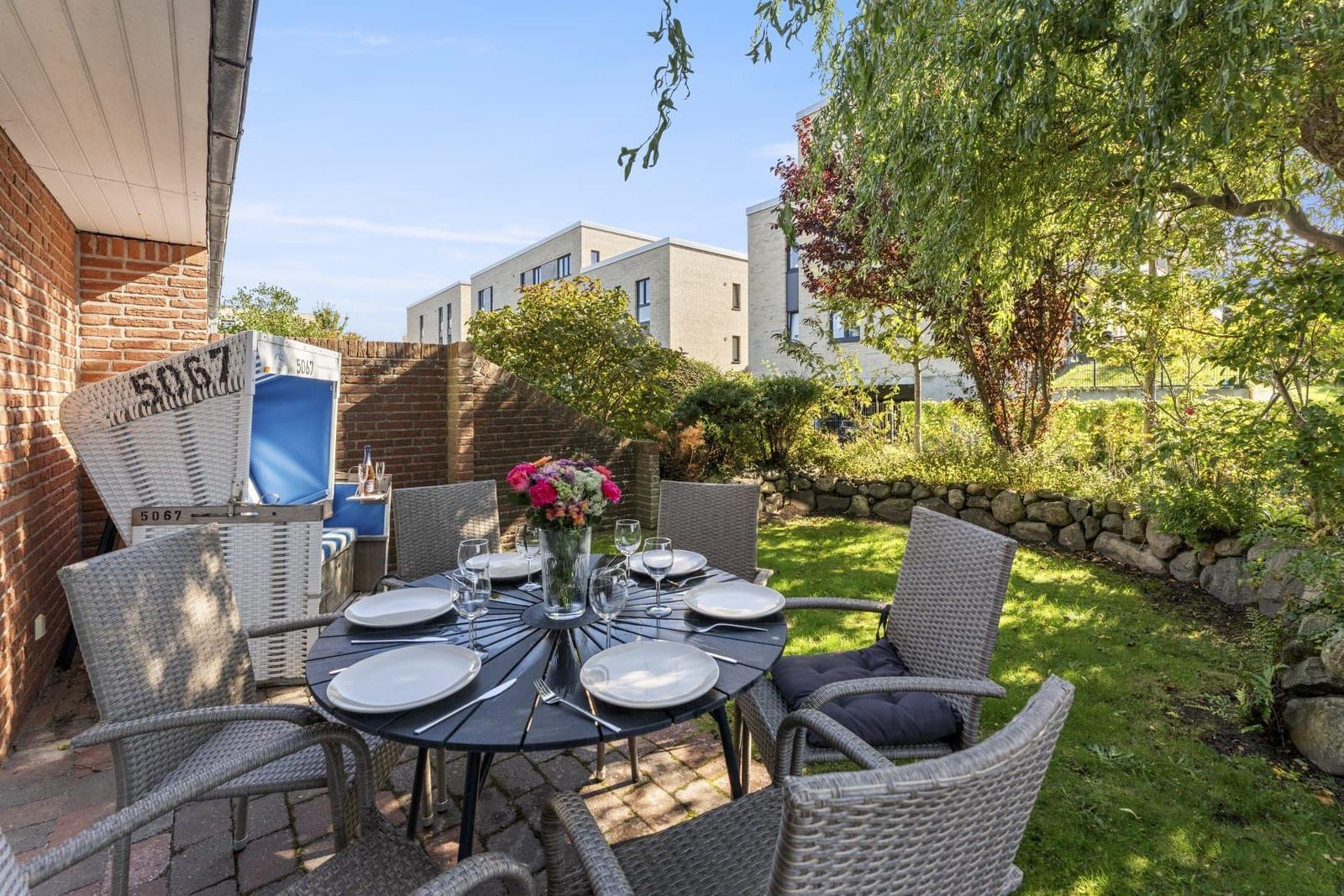 Garten mit runden Tisch, sechs Stühlen und Blumenarrangement.