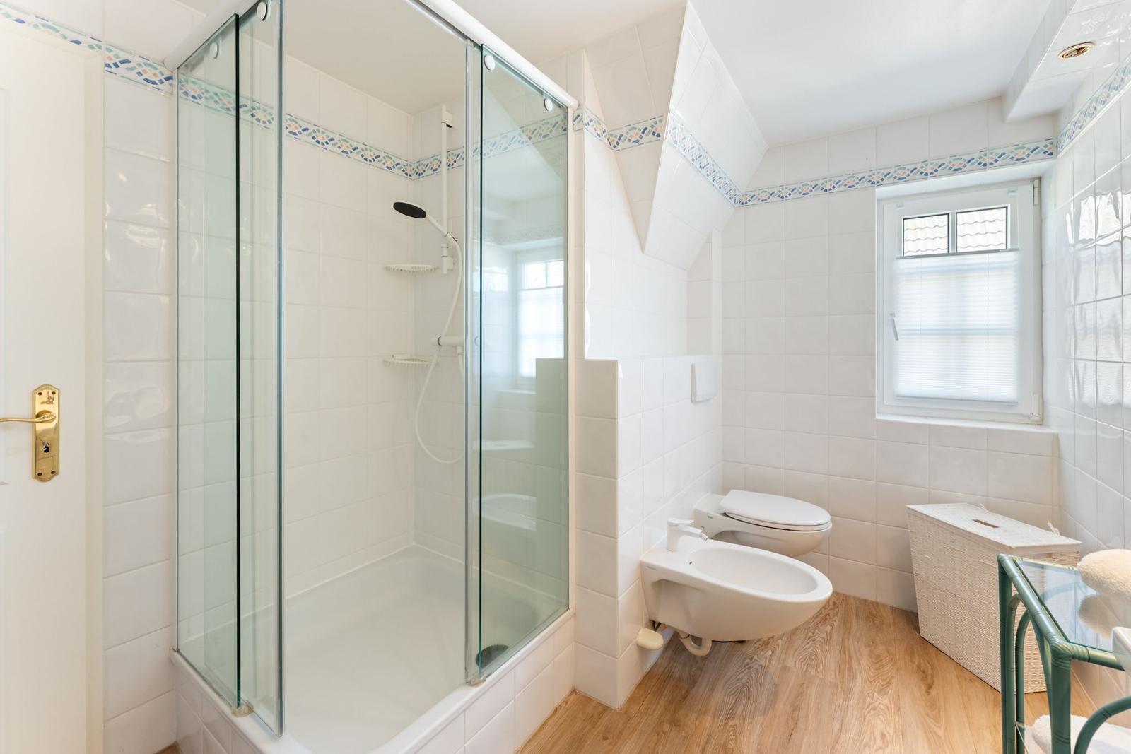 Badezimmer mit Dusche, WC und Waschbecken. Holzfußboden und Fenster.
