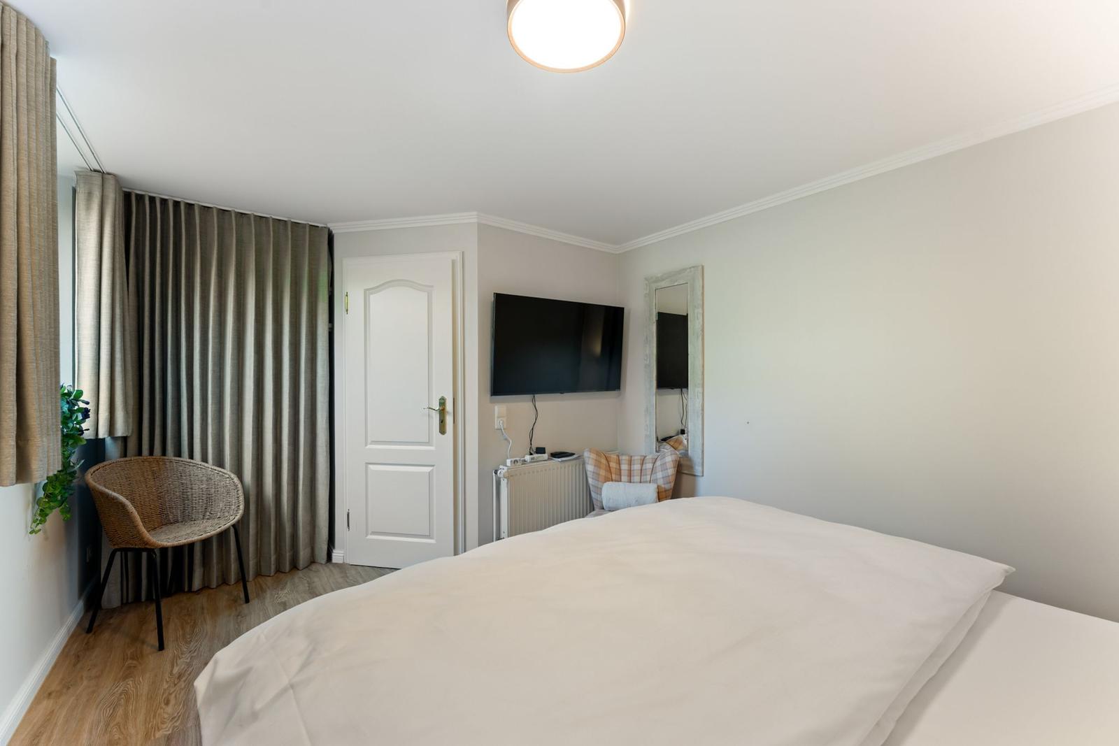 Schlafzimmer mit Bett, Fernseher, Spiegel und Stuhl.