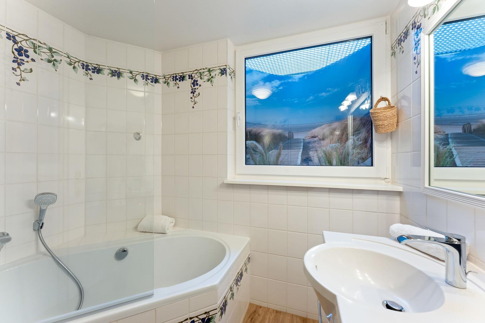 Badezimmer mit Badewanne, Waschbecken und Fenster mit Strandbild