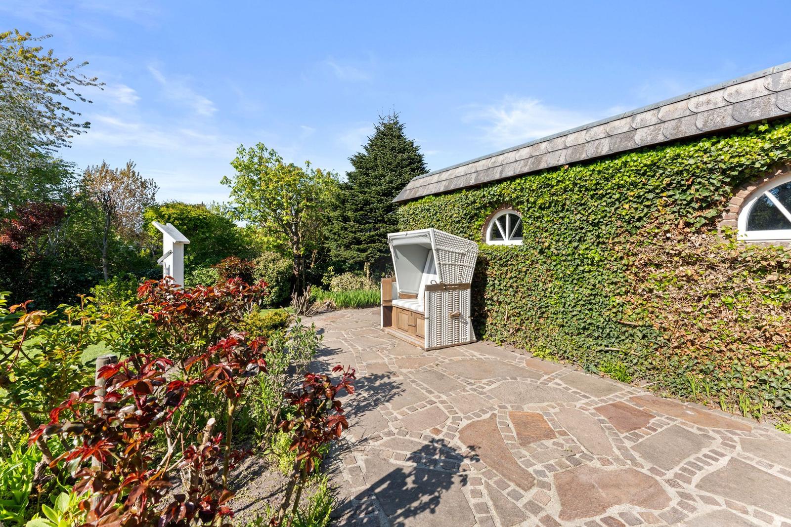 Gartenweg mit Steinplatten, grüner Wand und Liegestuhl.