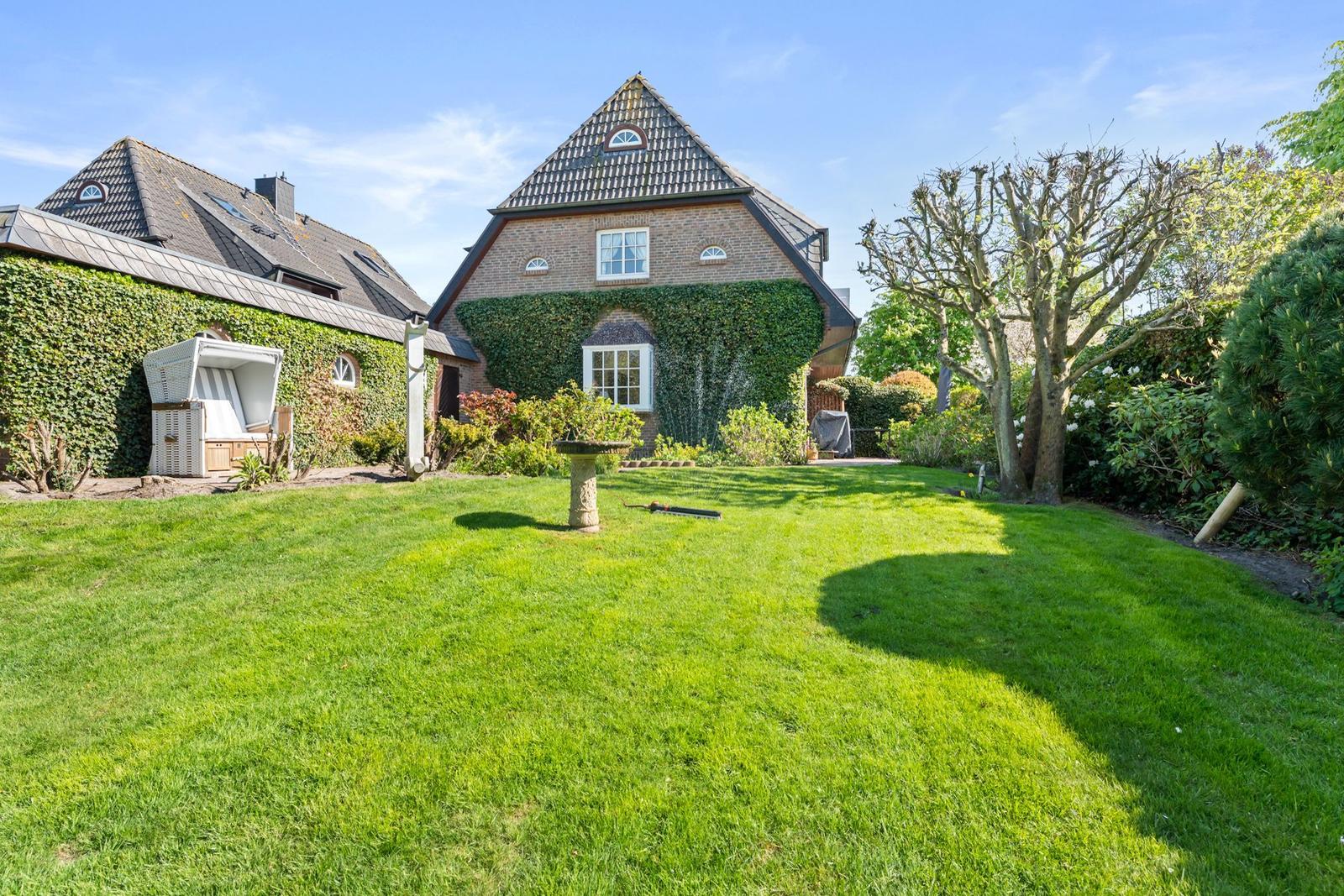 Haus mit grünem Garten, Kletterpflanzen und Terrasse im Hintergrund.
