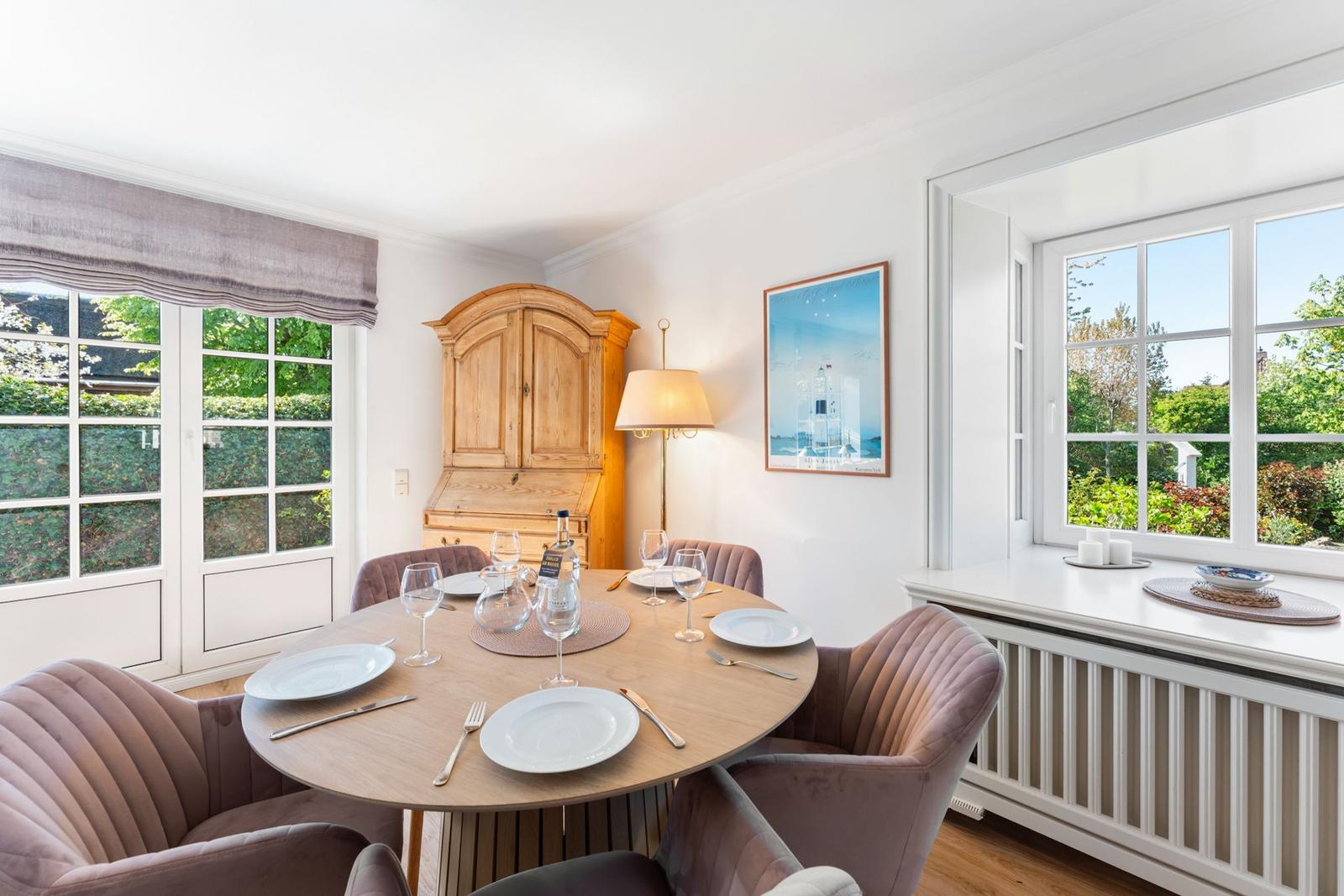 Rundtisch mit Stühlen, Holzschrank und Fenster mit Blick auf Garten.