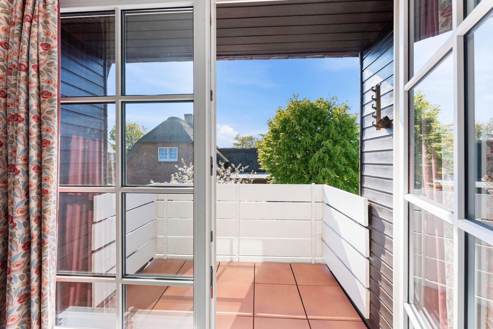 Terrasse mit weißem Zaun und roten Fliesen. Blick auf grüne Bäume und ein Haus mit Schieferdach.