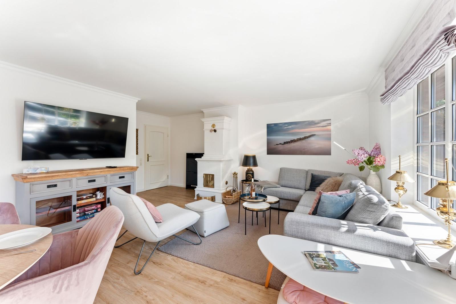 Wohnzimmer mit Sofa, Fernseher und Kamin. Fenster mit Blumen und Lampen.