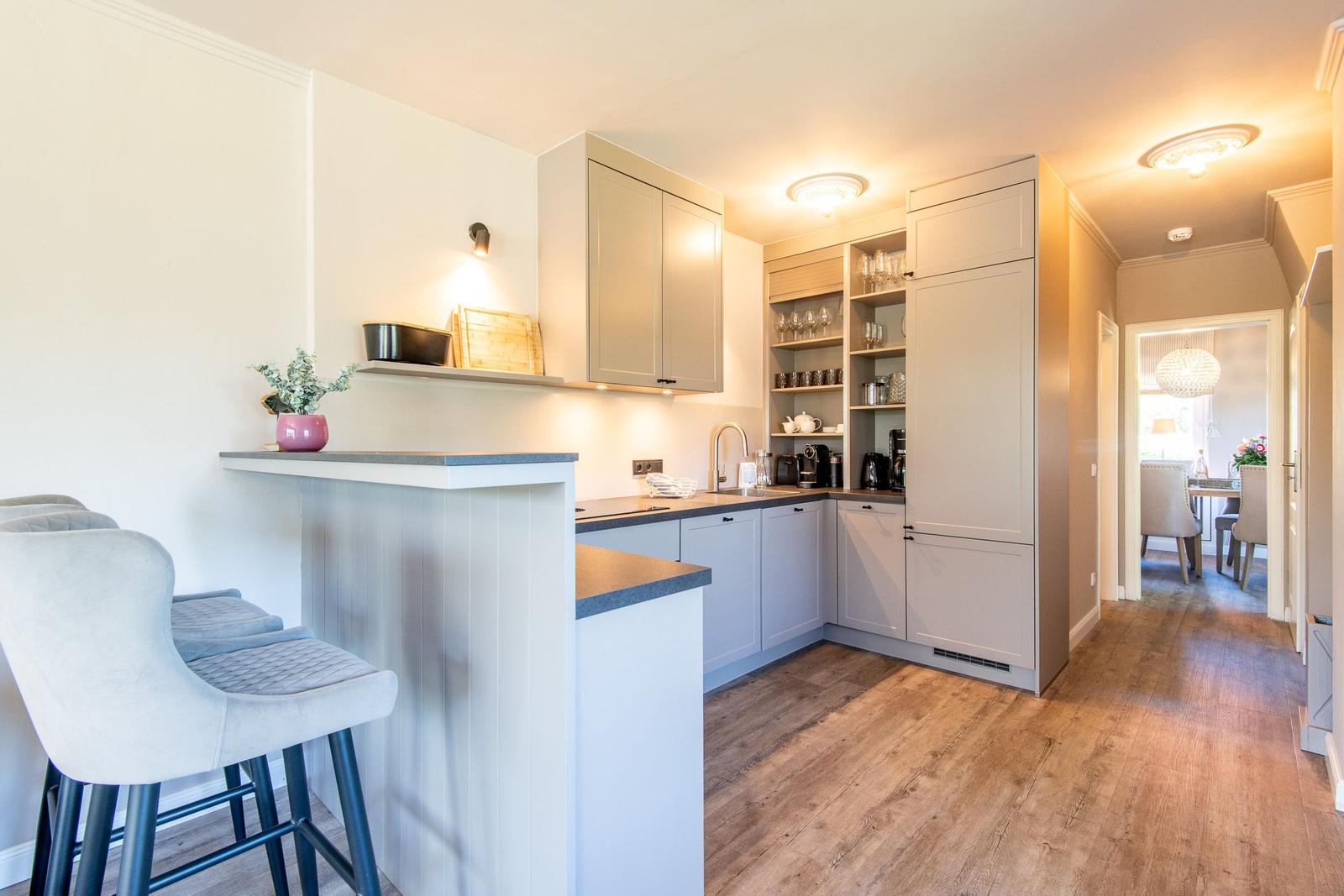 Küche mit Kücheninsel, Hochglanzschrank und Barhocker. Holzdielenboden und Blick in Esszimmer.