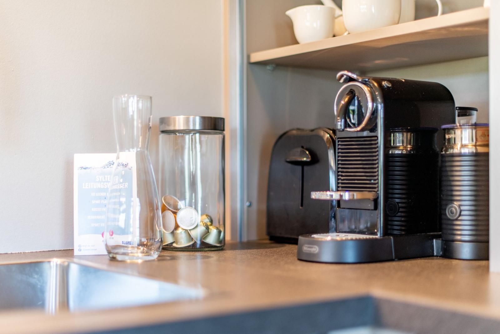 Küchenbereich mit Kaffeemaschine, Kapseln und Wasserkaraffe.