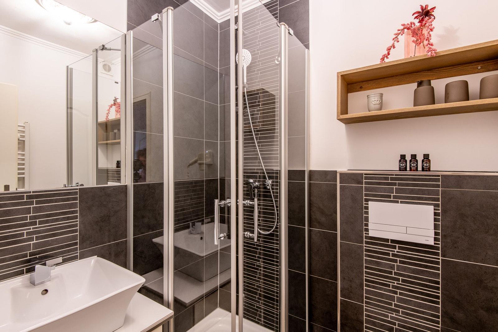 Dusche mit Glaswand, Waschbecken und Holzregal an der Wand.