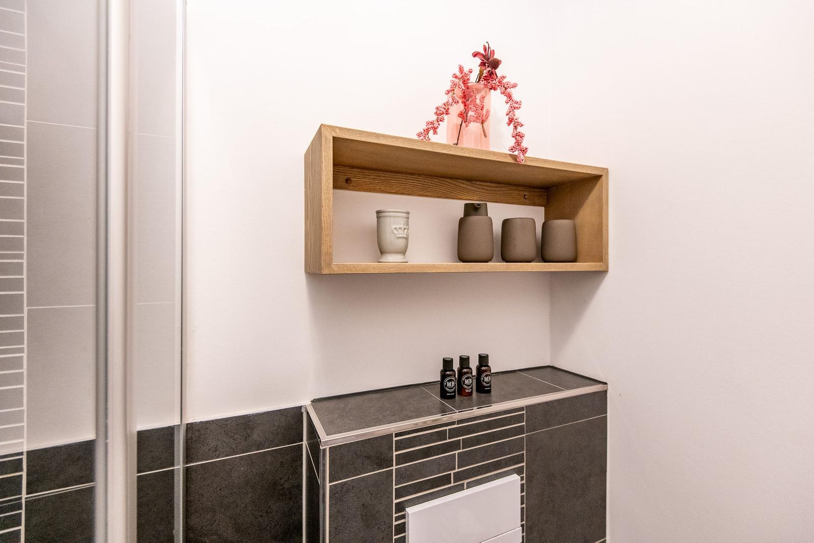 Wandregal mit Vasen und Pflanze über Waschbecken mit Duschwand