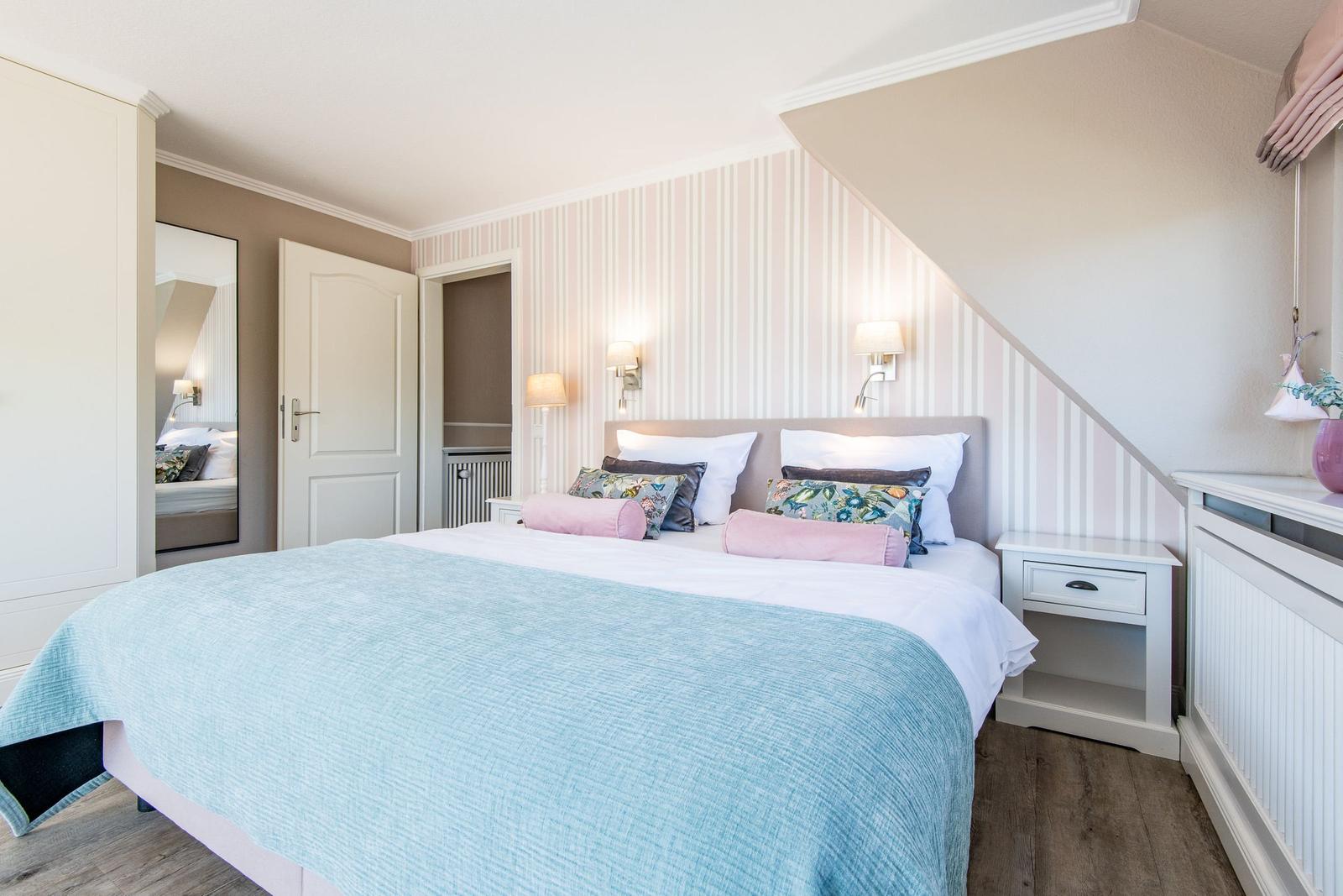 Schlafzimmer mit Bett, Nachttisch und Wandverkleidung. Tür und Spiegel sind sichtbar.