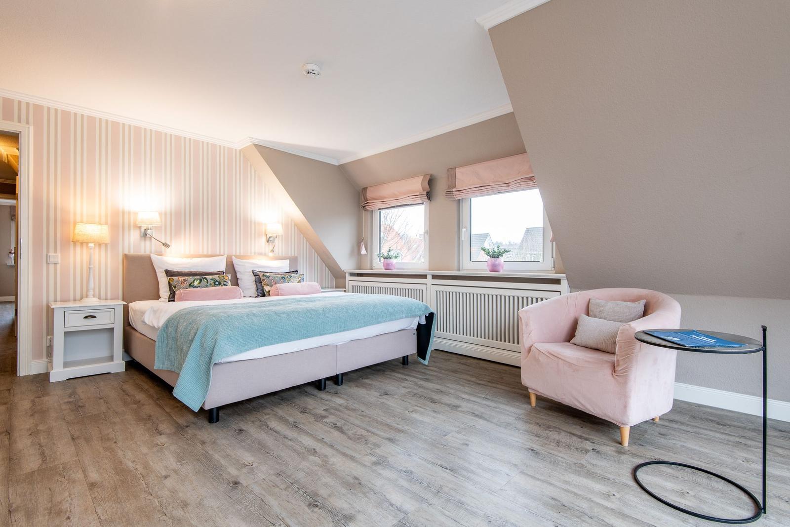Schlafzimmer mit Bett, Sessel und zwei Fenstern an schräger Wand.