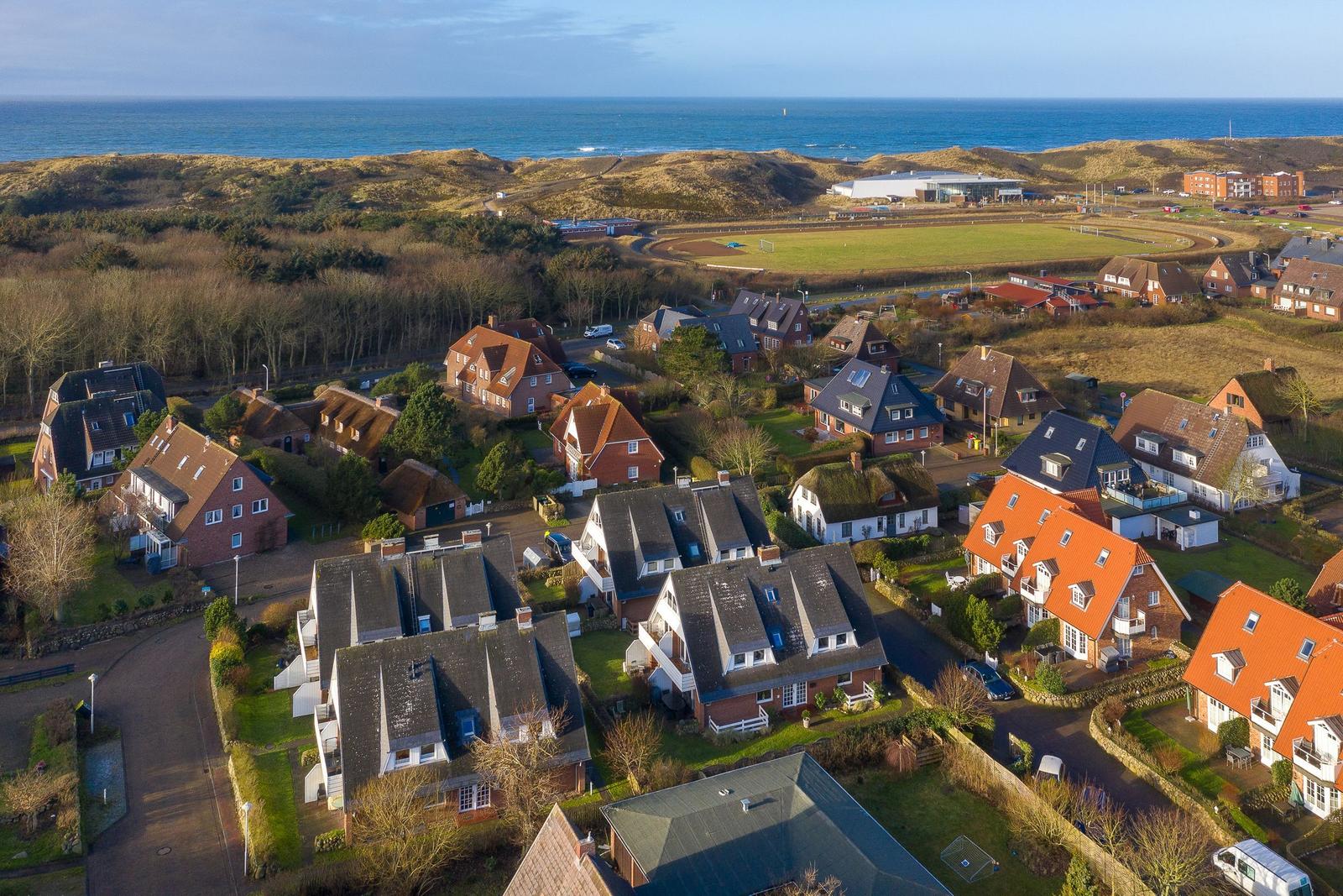 Aerial view of coastal village with houses, green fields, and ocean in background.