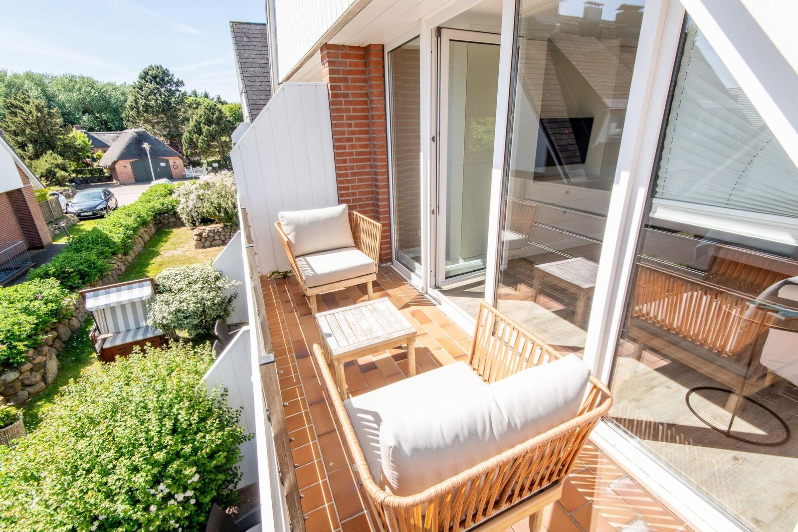 Terrasse mit zwei Sesseln und Tisch. Blick auf grünen Garten und Häuser.