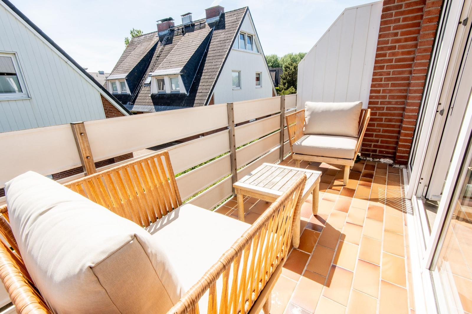 Terrasse mit zwei Sitzgelegenheiten und Tisch. Blick auf Nachbarhäuser und Grünflächen.