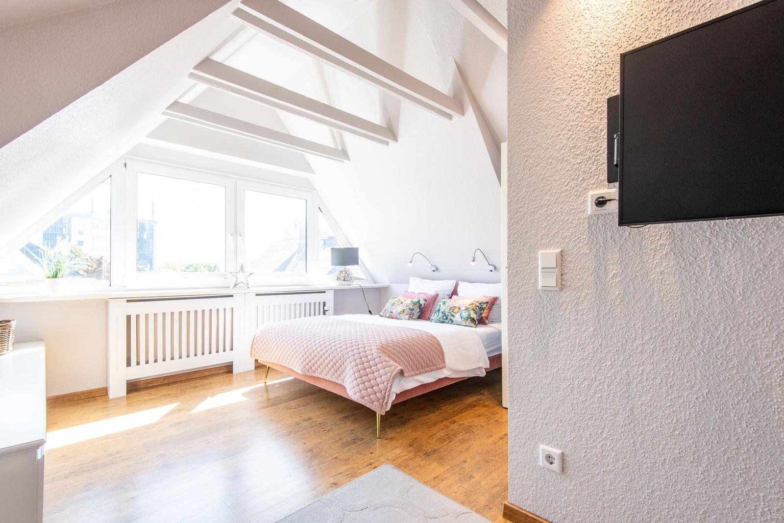 Schlafzimmer mit Dachschräge, Fenster und Bett mit rosa Decke.