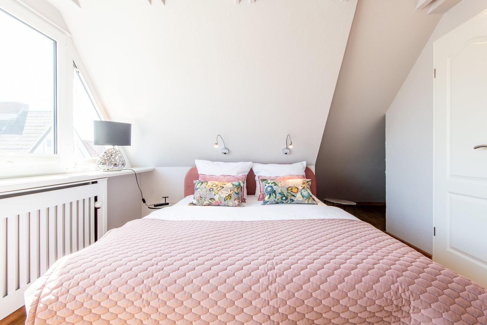 Schlafzimmer mit Dachschräge, Bett mit rosa Bettwäsche und Fenster mit Blick.