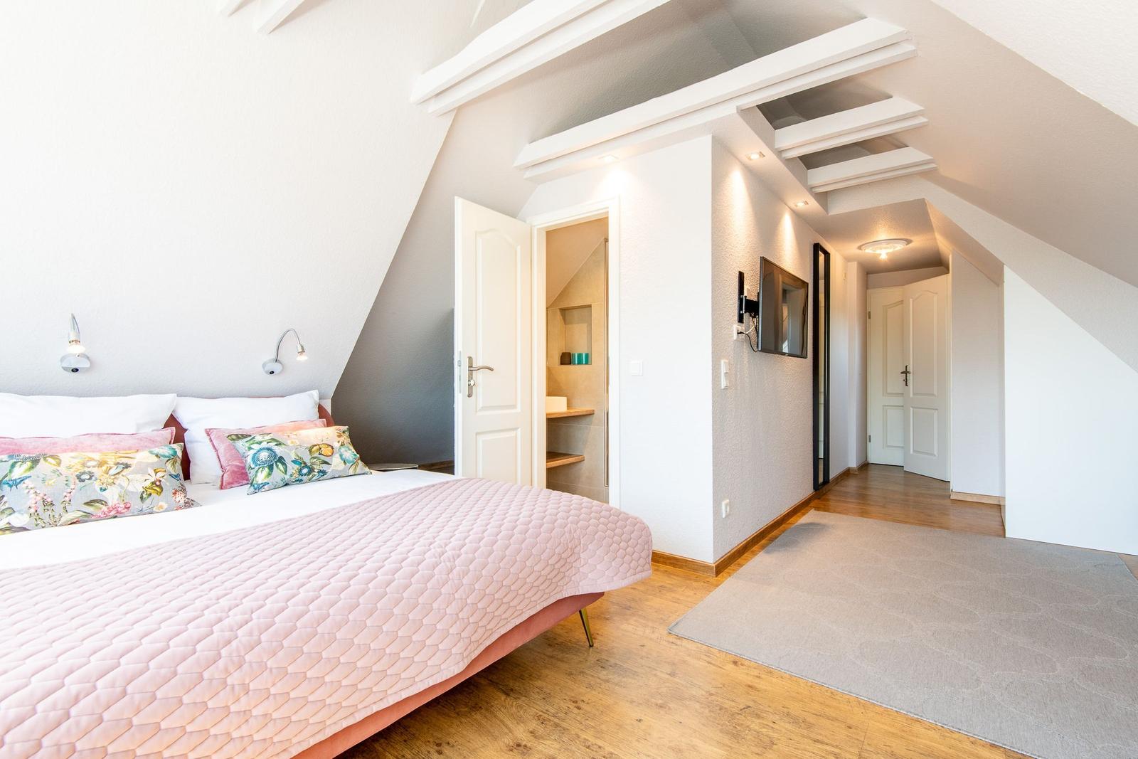 Schlafzimmer mit Bett, TV und angrenzender Dusche.