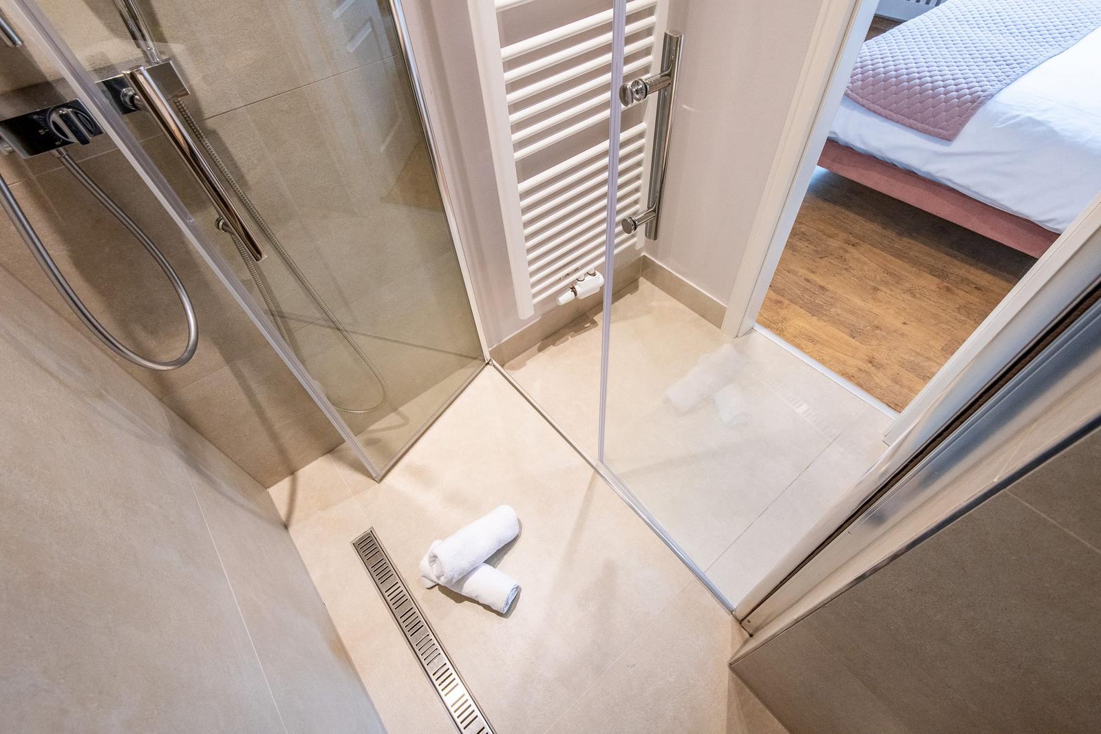 Dusche mit Glaswand, Handbrause und Handtuch auf dem Boden