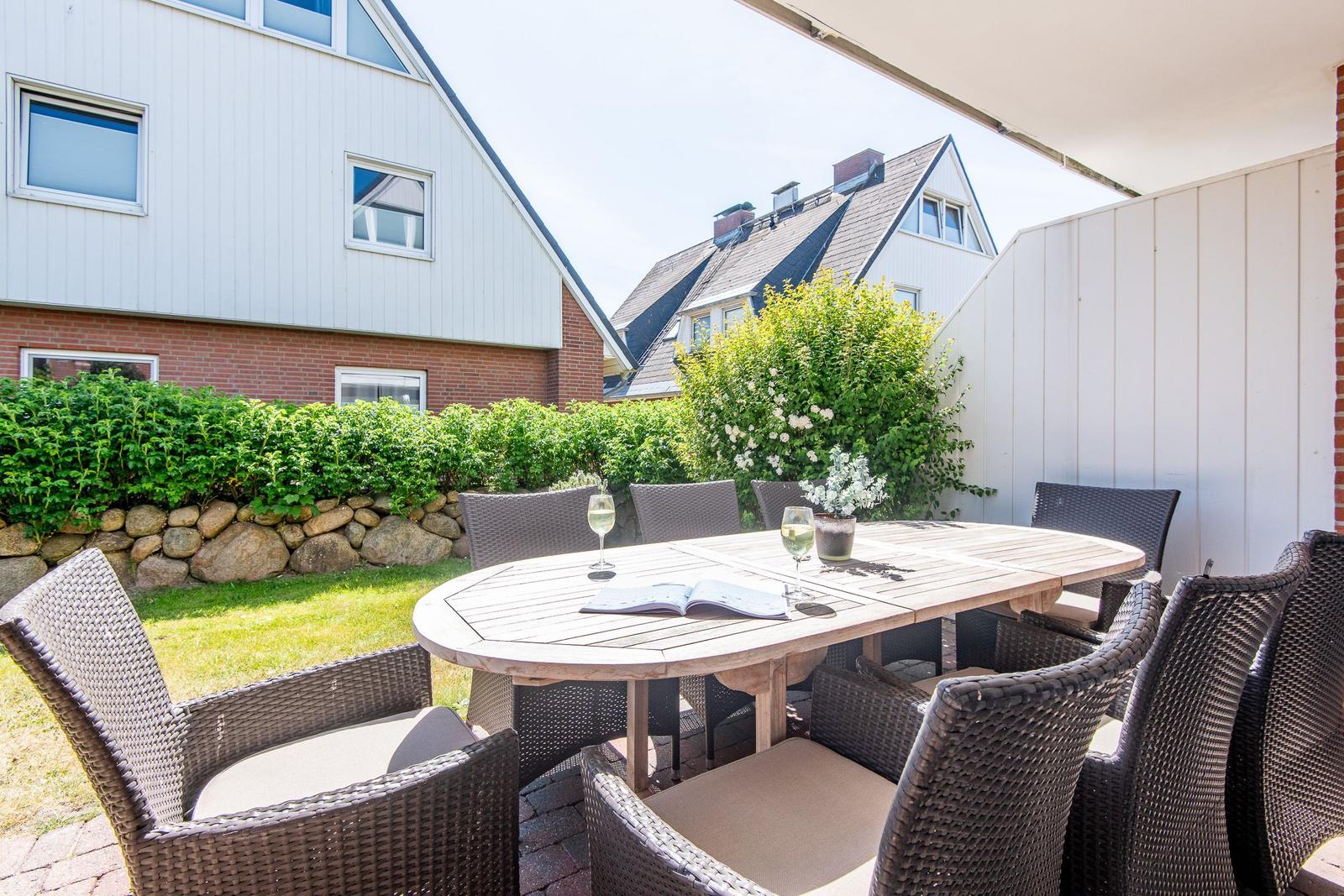 Terrasse mit Tisch und Stühlen, umgeben von Grün und Häusern.