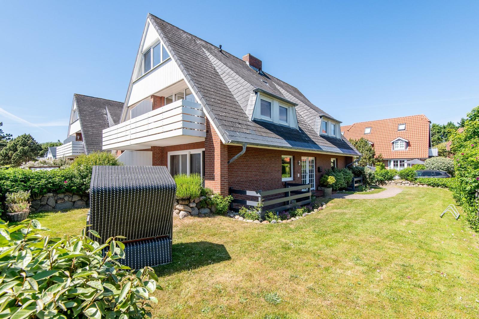 Ferienhaus mit Balkon, Garten und Terrasse unter blauem Himmel.
