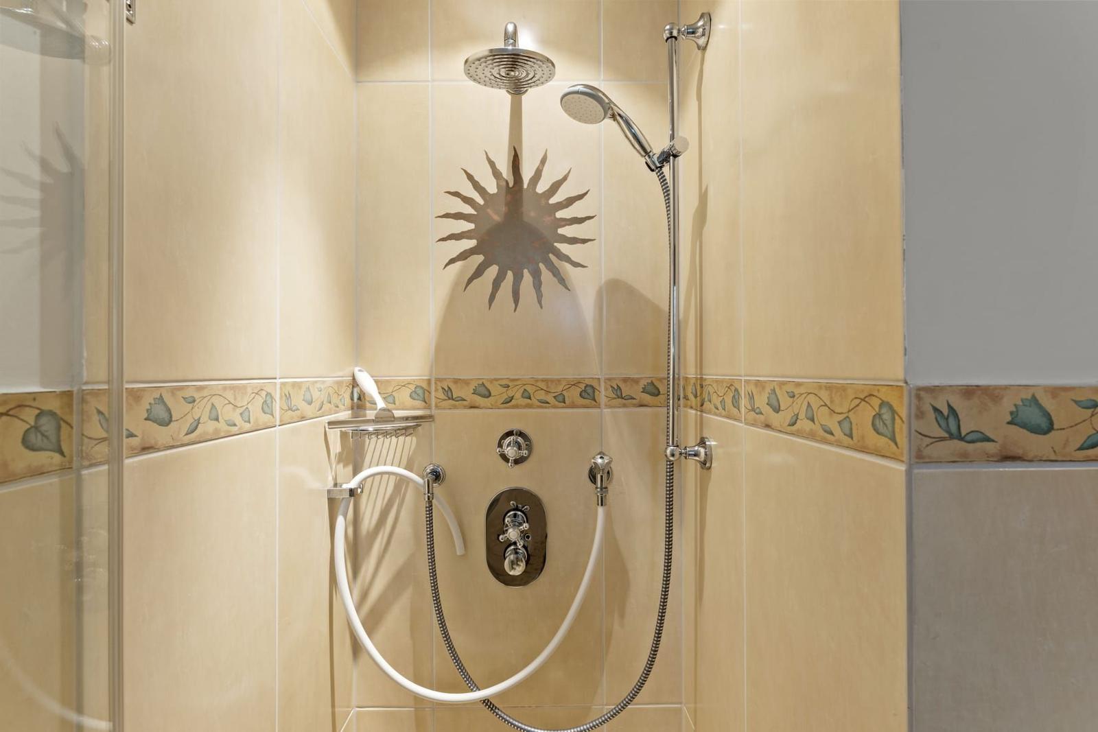 Dusche mit Duschbrause, Handbrause und Sonnenmotiv auf Wandfliese.