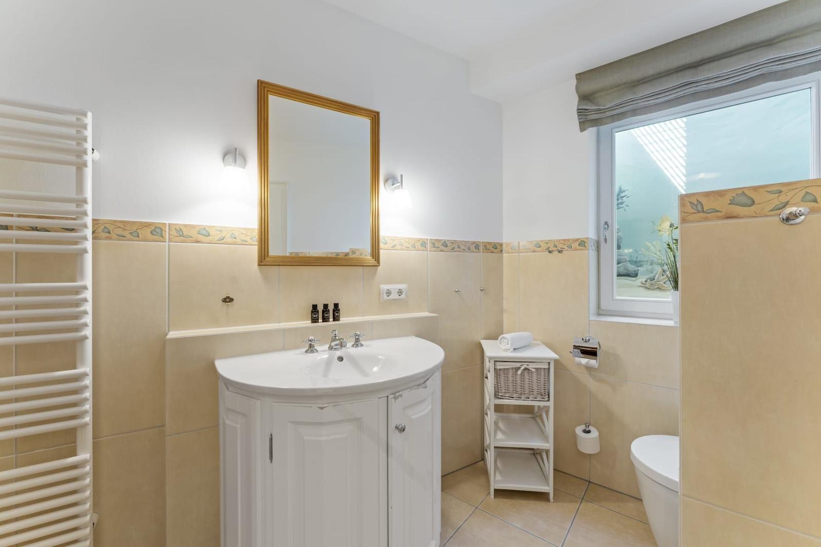 Badezimmer mit Waschbecken, Spiegel, Toilette und Fenster
