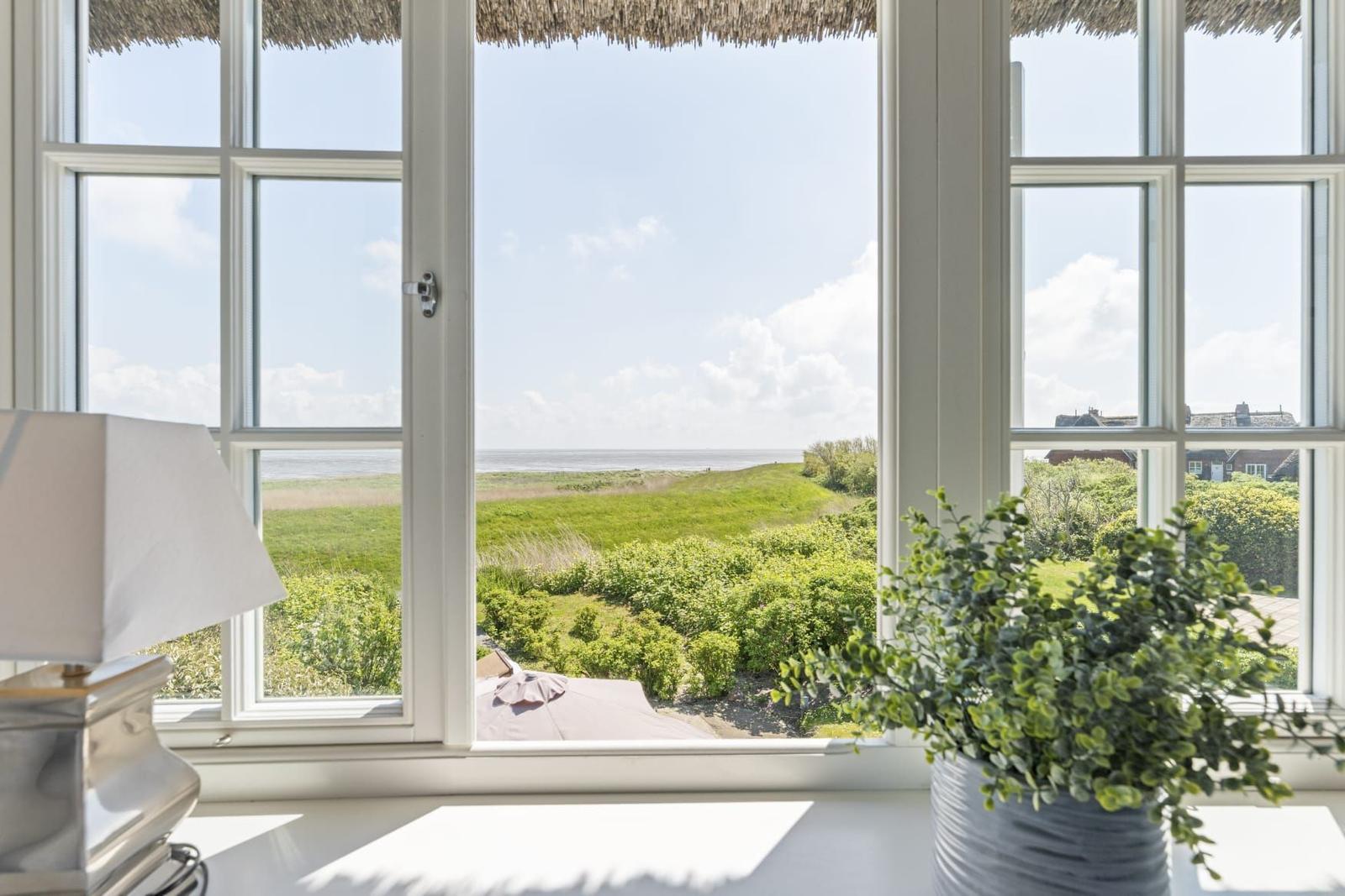 Durch das Fenster blickt man auf eine grüne Landschaft und das Meer.