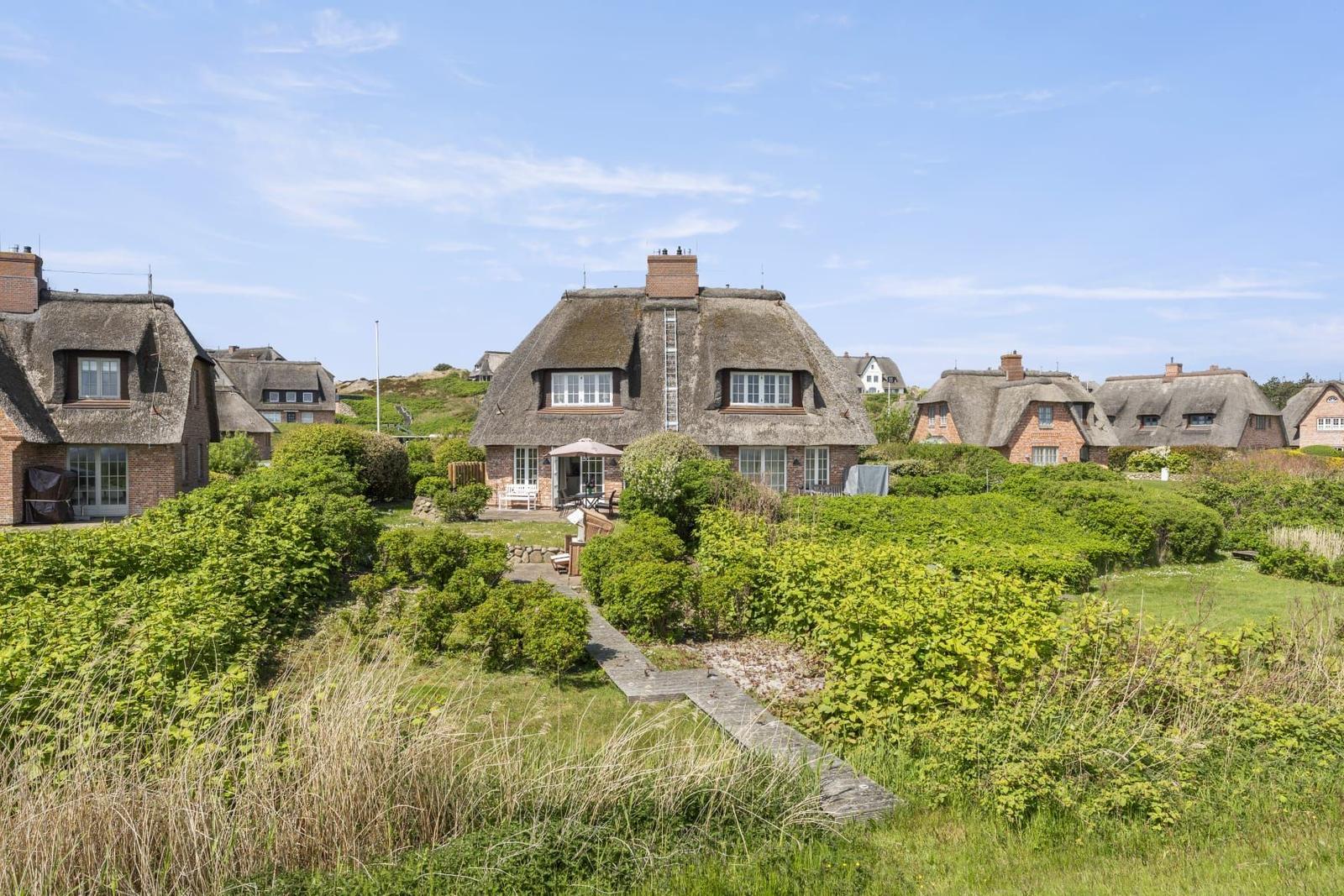 Haus mit Strohdach und Gartenweg unter blauem Himmel.