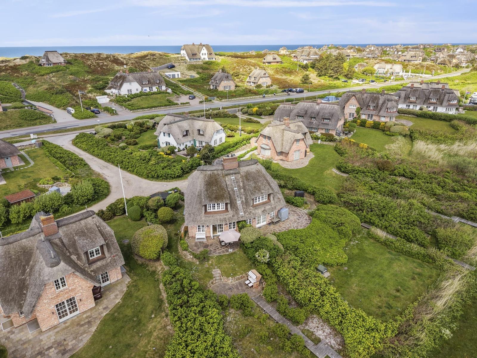 Dorf mit strohgedeckten Häusern und grünen Gärten am Meer.