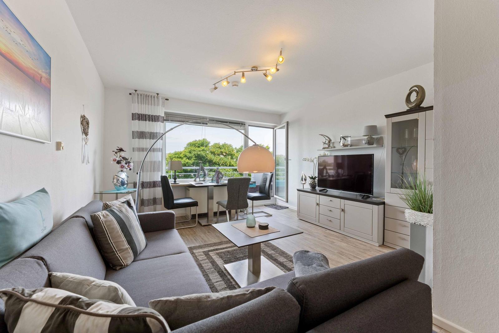 Living room with sofa, TV, and dining area. View to balcony with garden.